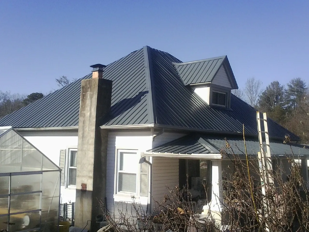 Dark blue standing seam metal roof on a white farmhouse with dormer — Slate & Tile Roof Repair by Roofing Brothers in Sacred Heart