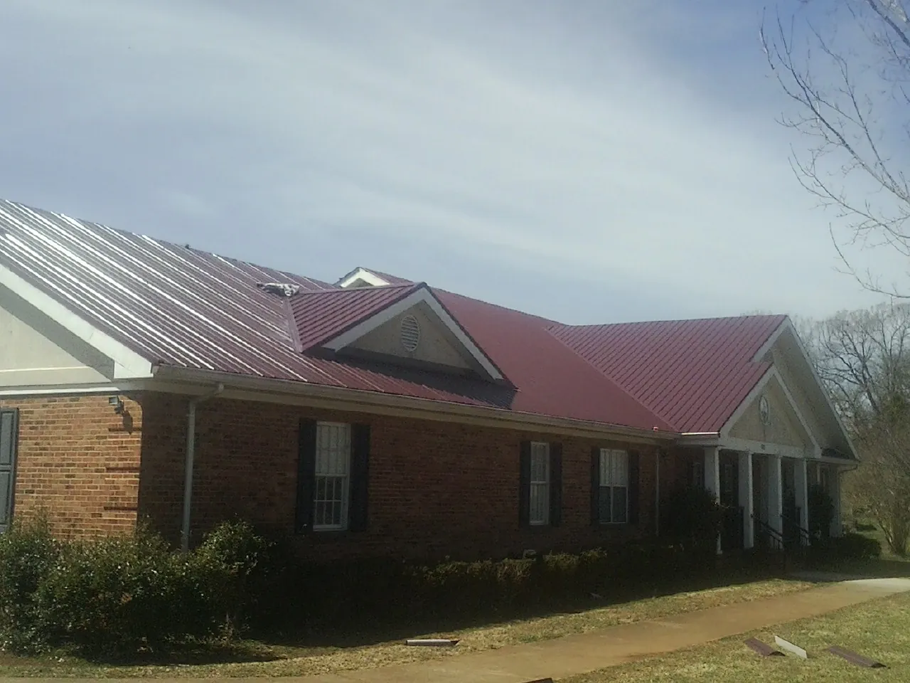 Red metal roof with gabled entries on a long brick building, from a Hail Damage Roof Repair job in Sacred Heart