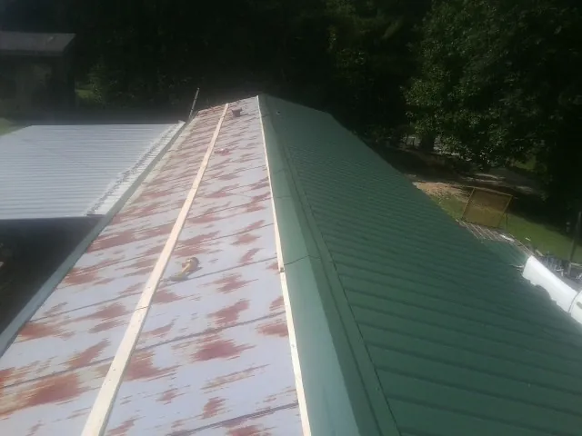 Old rusted panels beside newly installed green metal roofing — Wind Damage Roof Repair by Roofing Brothers in Sacred Heart