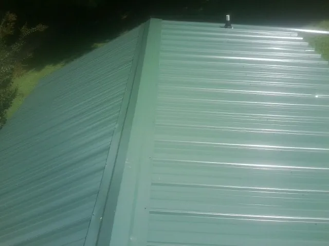 New green metal panels meeting at the ridge of a roof — Flat Roof Repair work by our crew in Sacred Heart