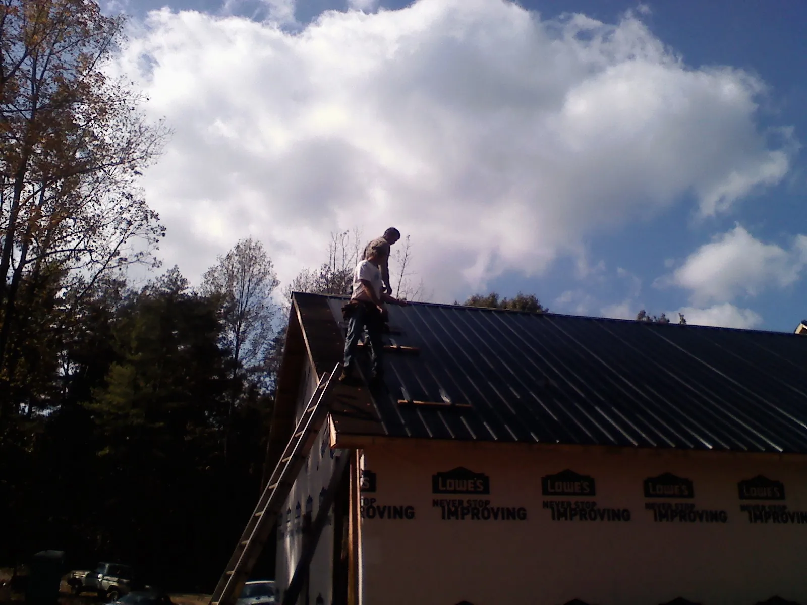 Roofer fastening dark metal panels high against a cloudy sky, from a Roof Inspection job in Sacred Heart