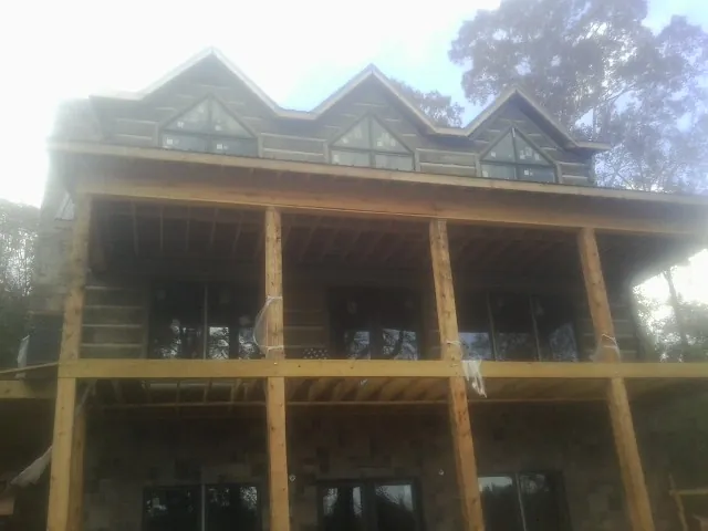 Dormers and porch framing on a large log home under construction — Roof Coating work by our crew in Sacred Heart