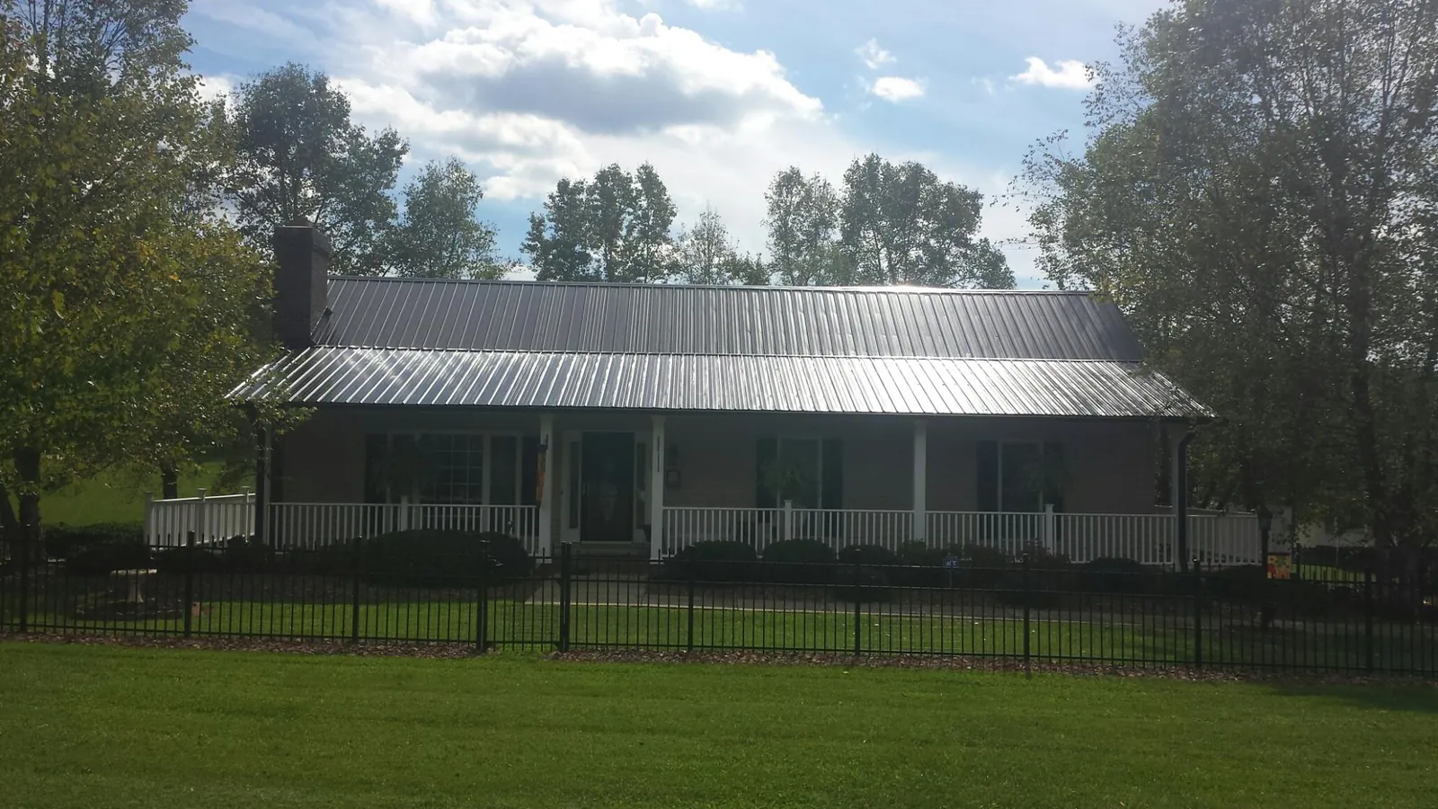 Gray metal roof on a brick ranch with a full width front porch — Gutter Guard Installation work by our crew in Sacred Heart