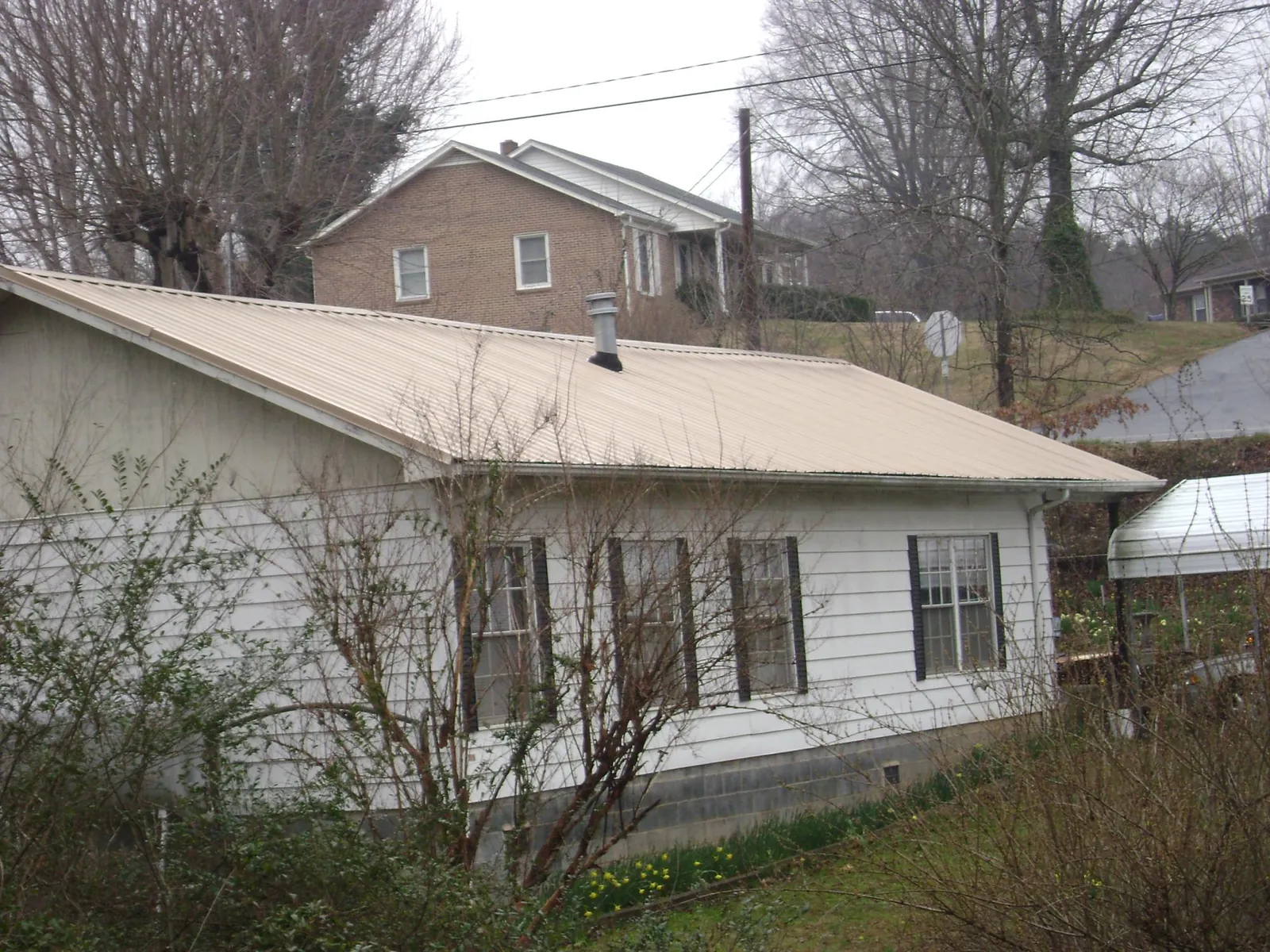 Tan metal roof on a white sided house set into a hillside — Commercial Roofing by Roofing Brothers in Sacred Heart
