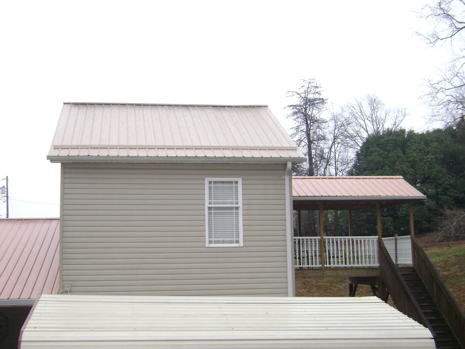 Tan metal roofs on a two story addition and attached porch, from a Roof Replacement job in Sacred Heart